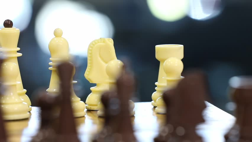 Close-up footage of two players making opening moves in a chess game. Hands strategically position white and black pieces on the wooden chessboard, initiating the intellectual battle.