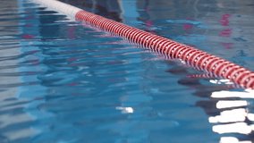 Close-up of a red and white swimming lane rope floating on clear, refreshing blue water. Gentle ripples and bright light reflections animate the tranquil pool surface. - Powered by Shutterstock - Get 15% off with code: PIKWIZARD15