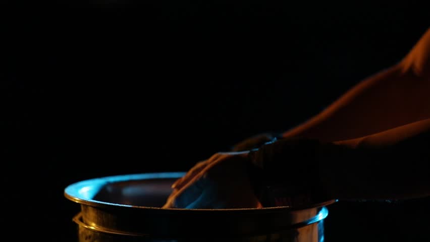 Close-up: Hands clap, creating a cloud of chalk over a metal container. Dramatic yellow and blue rim lighting highlights slow-motion particle dispersion.