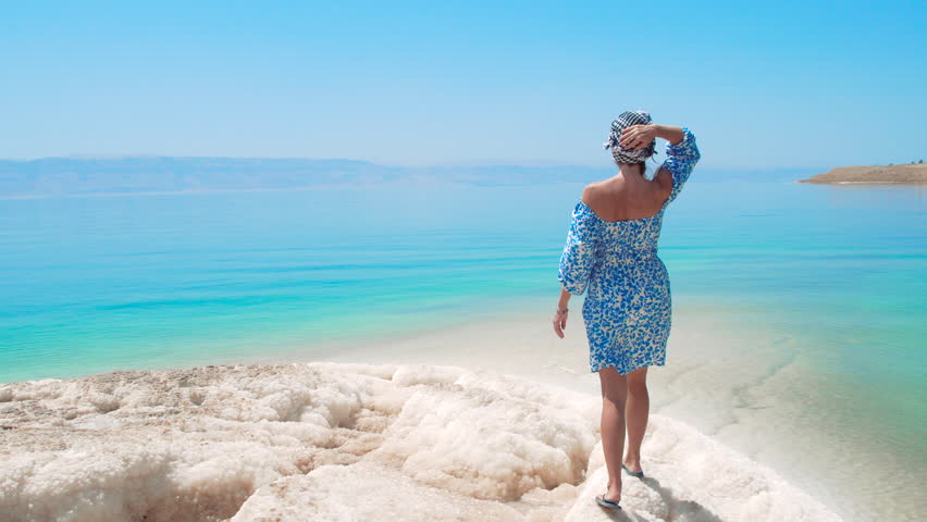 Woman walking on unique salt formations by the turquoise water of the Dead Sea, Jordan.