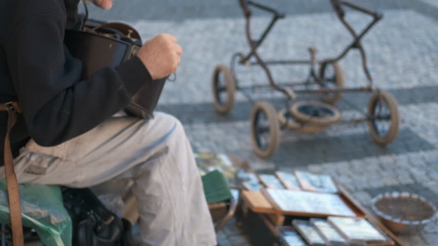 Street musician playing hurdy-gurdy in town square. Experienced musician performing traditional hurdy-gurdy music in historic town square, selling albums
