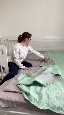 Caucasian woman spreading bedspread on bed. 