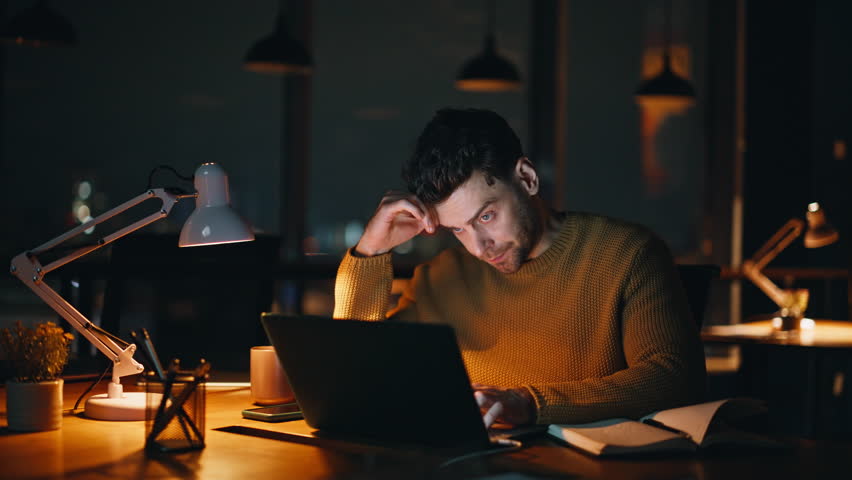 Overtime worker watching laptop looking solutions to work issues in dark workplace closeup. Overloaded manager solving problems late evening. Tensed freelancer thinking on hard business task at night.