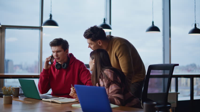 Happy staff overjoyed news hearing in cellphone at modern coworking space. Excited team members rejoicing business achievement calling phone. Smiling colleagues giving five celebrate success together.