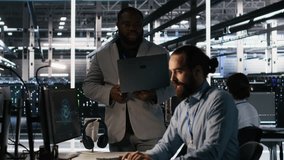 Data center engineers use laptop, collaborating on doing AI software updates. Server room teamworking colleagues doing brainstorming, optimizing infrastructure using artificial intelligence, camera A - Powered by Shutterstock - Get 15% off with code: PIKWIZARD15