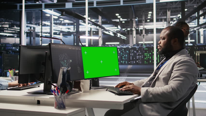 Data center admin inspecting gear using green screen mockup PC, doing maintenance tasks. African american server farm worker using chroma key computer, conducting system checks, camera A