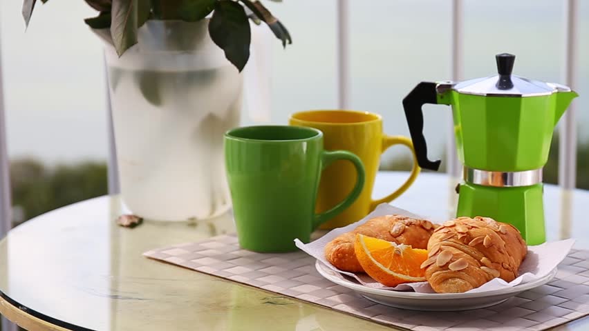 Delicious breakfast with coffee on hotel's balcony, fresh croissants and slice of orange fruit with coffee percolator background