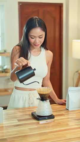 Young woman pouring hot water into pour over coffee dripper on a wooden kitchen counter