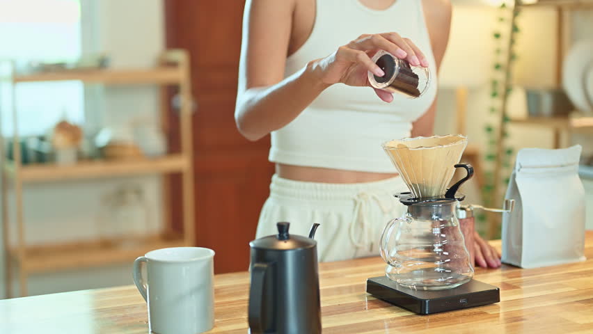 Close-up of hand pouring coffee grounds into a dripper on a wooden kitchen counter