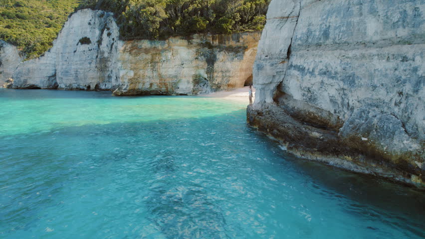 Woman jumping into turquoise waters at White Cliffs Beach Ionian Island Greece