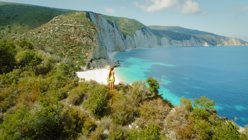 Tourist standing on a cliff overlooking Fteri Beach with blue waters in Kefalonia Greece