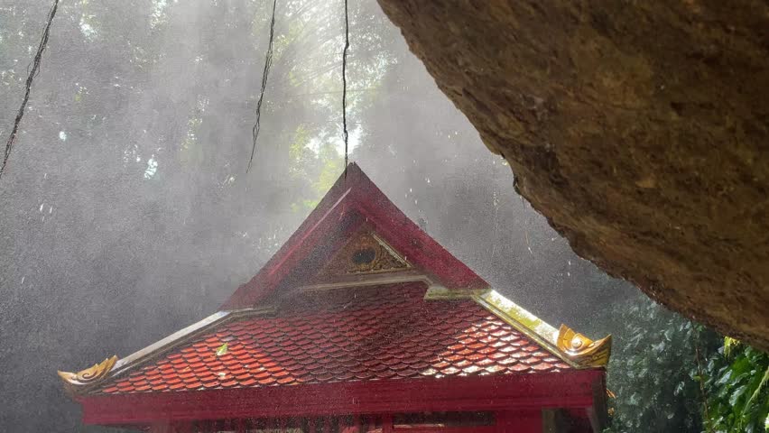 Water Mist Cooling Traditional Structure Near Rock Outcrop,"Gentle water mist cools a traditional structure with red tiled roof near a natural rock formation, creating a serene and refreshing atmosphe
