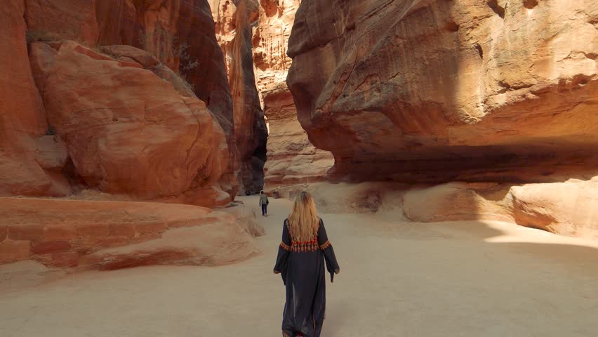 View of a person walking along a sandy path through the narrow Siq canyon rock formation towards Petra, Jordan.