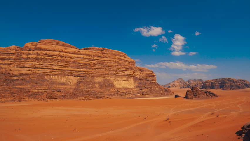 Wide view of a desert landscape with red sand and large rock formations under a blue sky, resembling the terrain of Mars. Wadi Rum, Jordan.