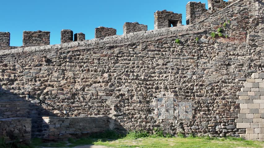Ancient stone walls of Monsaraz Castle standing tall against a vibrant blue sky, showcasing medieval architecture in the heart of Portugal
