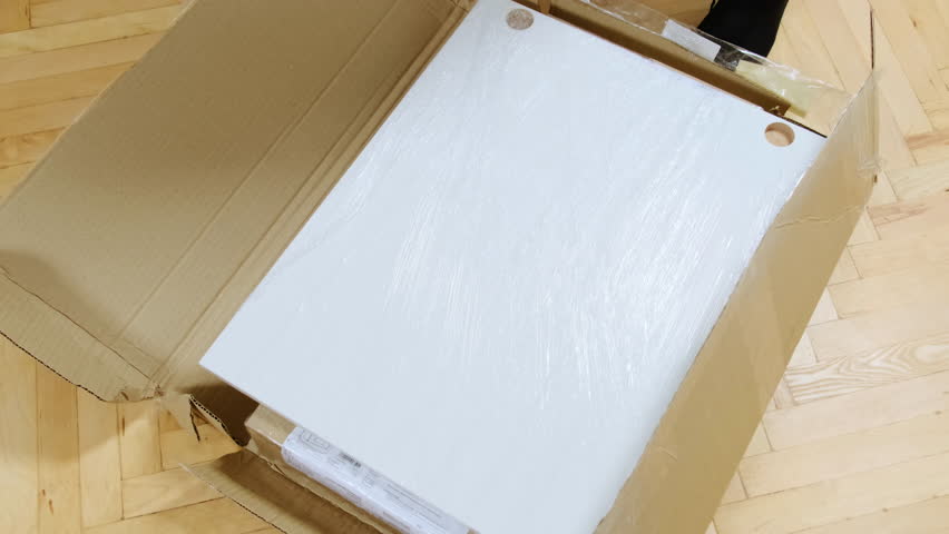 Man hand takes cardboard sheets out of open box on floor closeup. Guy unpacks parcel with items for furniture assembly in carton package at home. Unboxing video