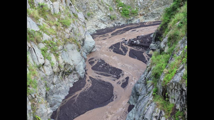 View of a murky river with rocky cliffs overgrown with grass.