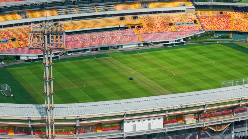 Aerial orbit establishing a person with heavy machinery mowing the lawn of the empty El Campin stadium in Bogota, Colombia on a sunny day.