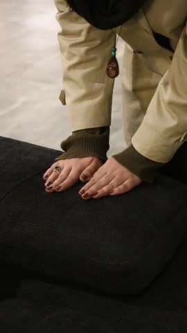Close-up of a hand touching the armrest of a dark sofa to feel fabric quality. Textured upholstery and fine weave pattern visible. Neutral showroom interior in soft focus. Person assesses comfort
