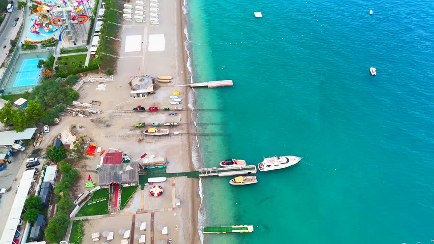 Aerial drone shot lowering over beach resort with docked yachts, water sports zone and nearby seaside water park