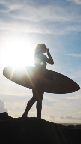 Sunset Silhouette Of Female Surfer Holding Board Standing On Rock Slow Motion Vertical Surf Scene With Sunflare