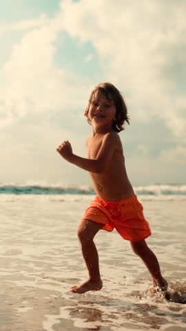 Smiling Boy Running Through Ocean Water on Family Vacation