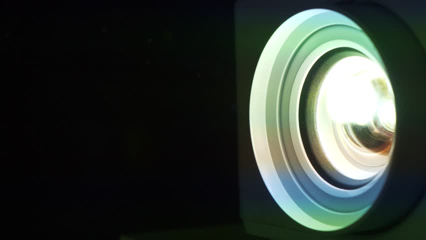 Movie is shown through projector. Light passes through lenses. Projector lens in operation in cinema hall. Lenses of working projector change color