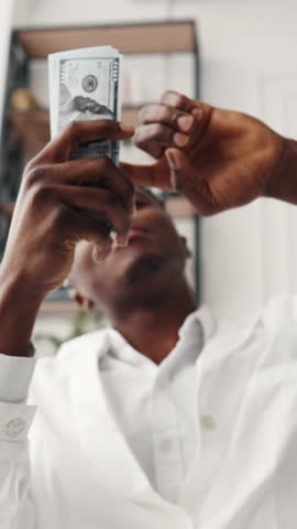 Rich health professional throwing money in air, vertical video with african american male person, new dollars banknotes, happiness and joy, millionaire dentist rejoicing by his salary in modern clinic