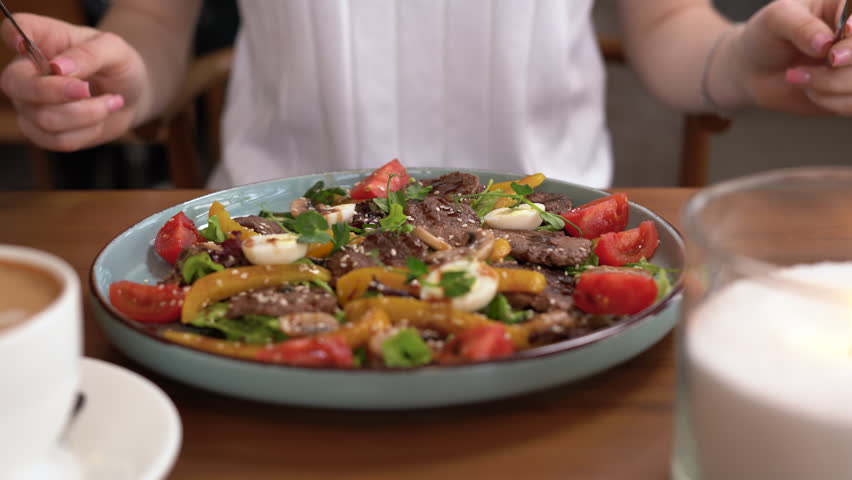 Woman eating hot beef salad with tomatoes, eggs and pepper in plate, close-up. Healthy food