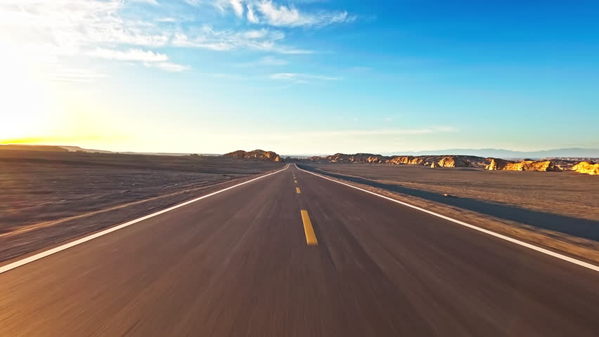 Asphalt road leading through a desert landscape at sunset. Driving car on a desert road.