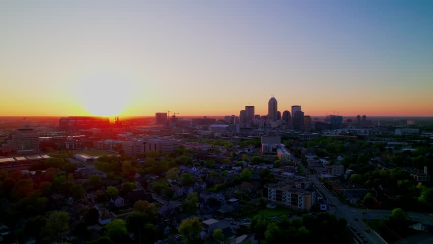 Aerial footage captures a breathtaking sunset over Indianapolis, Indiana, showcasing the city skyline illuminated by vibrant, warm evening light.