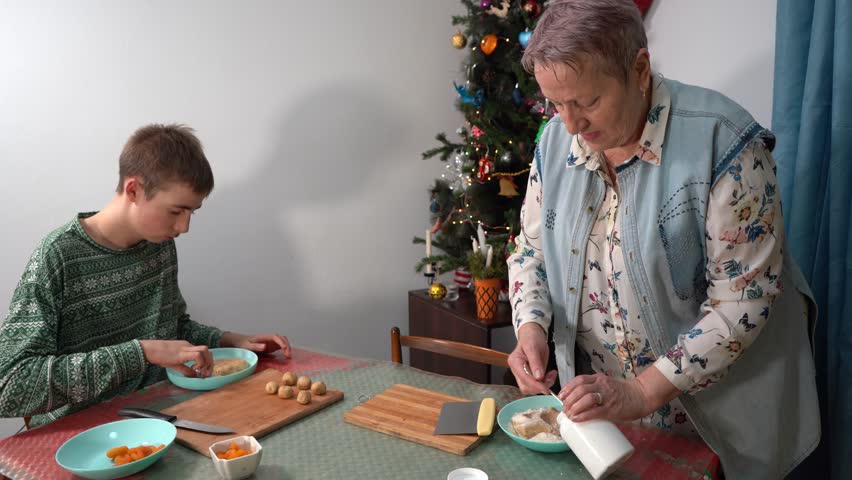Making fruit pies. A boy and his grandmother baking Christmas pastries. An elderly woman and a teenager cooking food at the kitchen table. Cookies bake