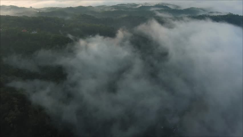 Drone shot of scenic mountain landscape wrapped in clouds at dawn, camera slowly tilting up toward the golden sunlight.