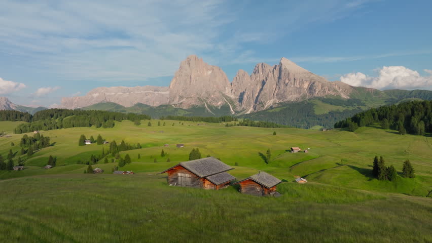 Aerial estabilshing of farm and meadows at Alpe di Siusi, Italy with mountain peaks at sunset