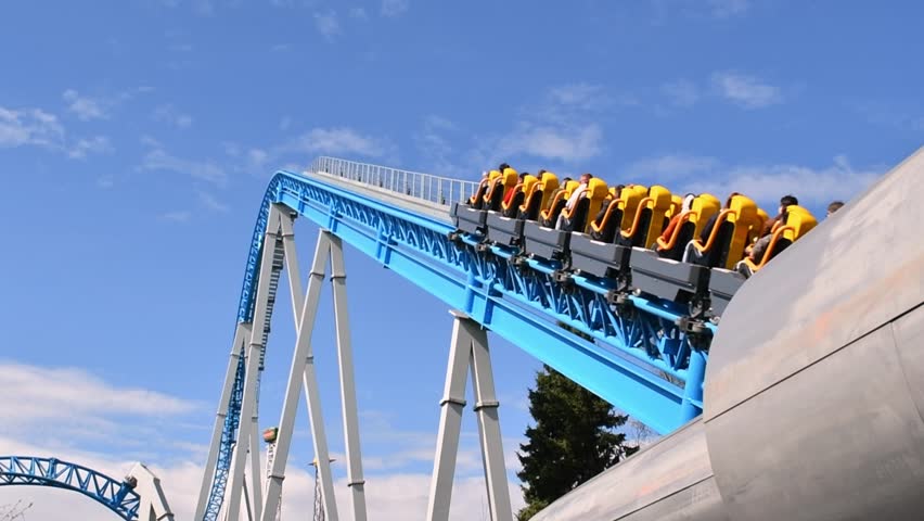 Roller coaster climbing blue track under clear sky with riders in yellow seats ready for thrilling drop in amusement park.