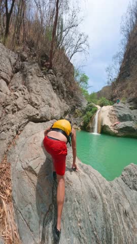 Tourist wearing a life jacket preparing to jump from a rock into the turquoise water of the magdalena waterfall in tlatlauquitepec, puebla, mexico