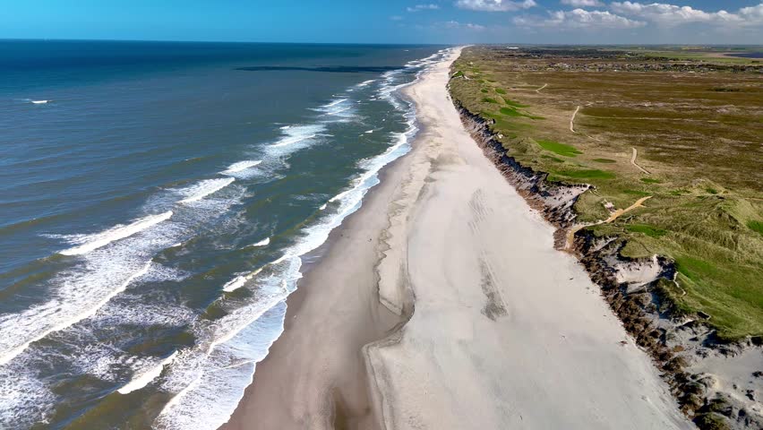 Waves lap gently against the sandy shores of Rubjerg Knude Fyr Lighthouse in Jutland, Denmark.