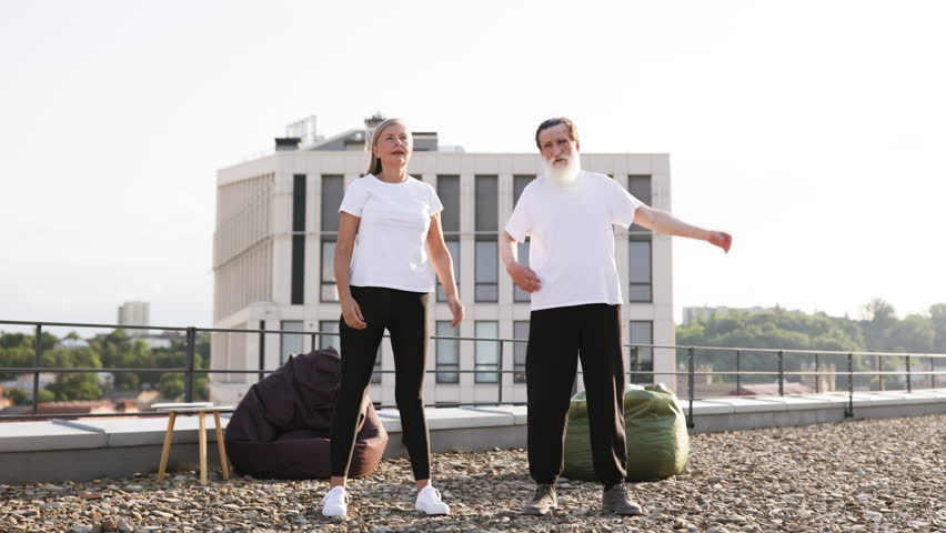 Elderly man and woman practicing yoga and stretching exercises on urban rooftop outdoors.