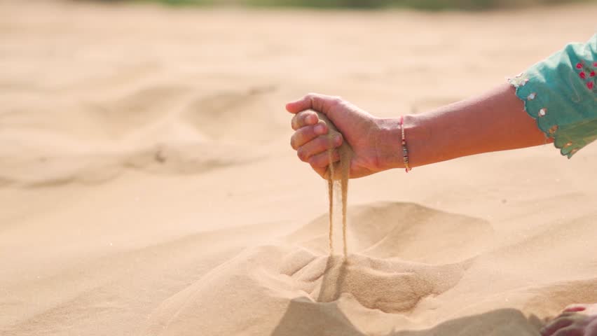 Close-up of Indian female hand releasing dropping sand in desert at Jaisalmer, Rajasthan, India. A girl holds hot sand in her hand. The concept of quickly passing time.
