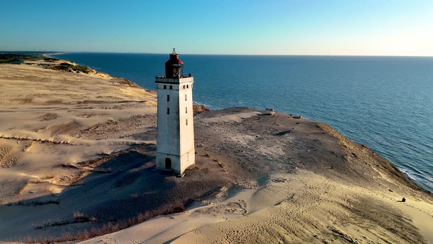 This captivating view showcases the historic lighthouse standing proudly against the backdrop of endless sands and the serene North Sea in Jutland, Denmark.mRubjerg Knude Fyr Lighthouse