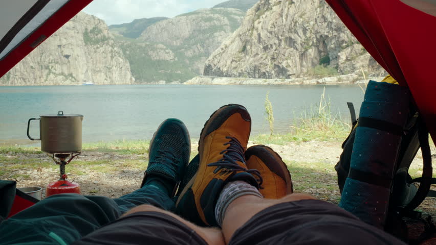 Peaceful Camping moment in Norway. Couple relaxes inside a red tent, enjoying stunning view of mountains and water. Tranquil outdoor experience surrounded by Nordic wilderness. 4K handheld medium shot