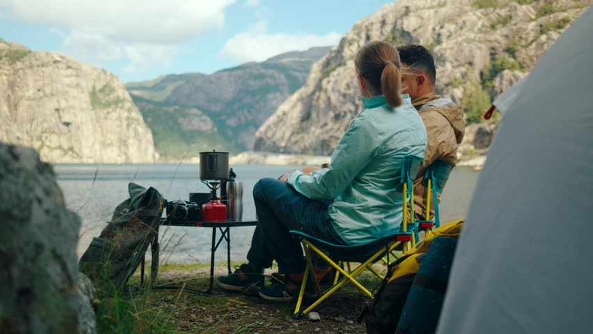 Couple camping by the bay in Norway, cooking on a stove and enjoying peaceful surroundings. Stunning landscapes, fresh air, and a cozy outdoor experience in the Nordic wilderness. 4K static wide shot