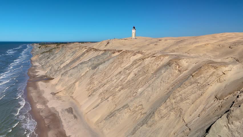 Breathtaking views of Rubjerg Knude Fyr Lighthouse in Jutland Denmark reveal its sandy dunes and rolling waves. Visitors enjoy a serene ambiance while the lighthouse