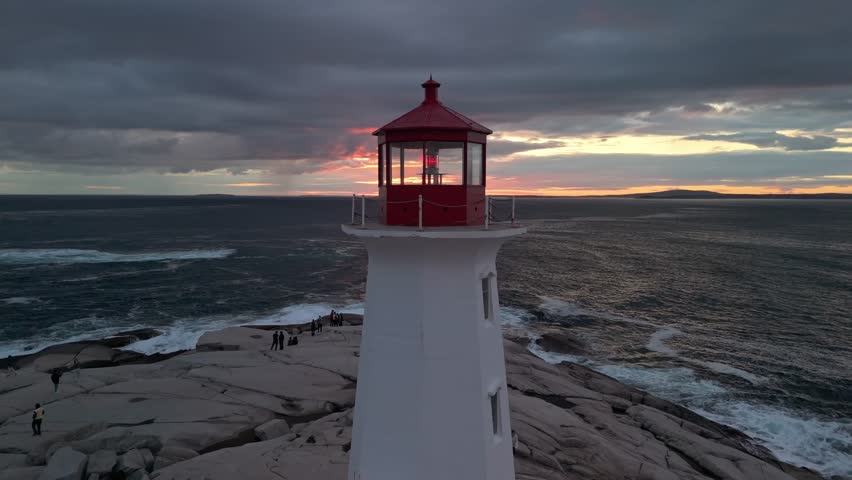 Aerial View Of Peggys Cove Near Halifax Shows The Iconic Lighthouse On A Rugged Shoreline, Surrounded By Roaring Waves Beneath A Stunning Coastal Sunset.
