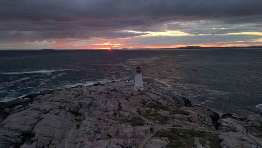 From An Aerial View Above Halifax, Peggys Cove Lighthouse Glows In Evening Light, Surrounded By Crashing Waves On The Rugged Atlantic Coastline. 
