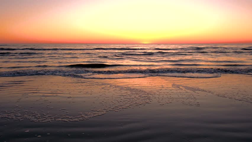 Breathtaking deep orange and pink hues paint the sky as the sun sets over Romo Lakolk Beach. Gentle waves lap at the shore, creating a serene atmosphere perfect for relaxation and reflection.