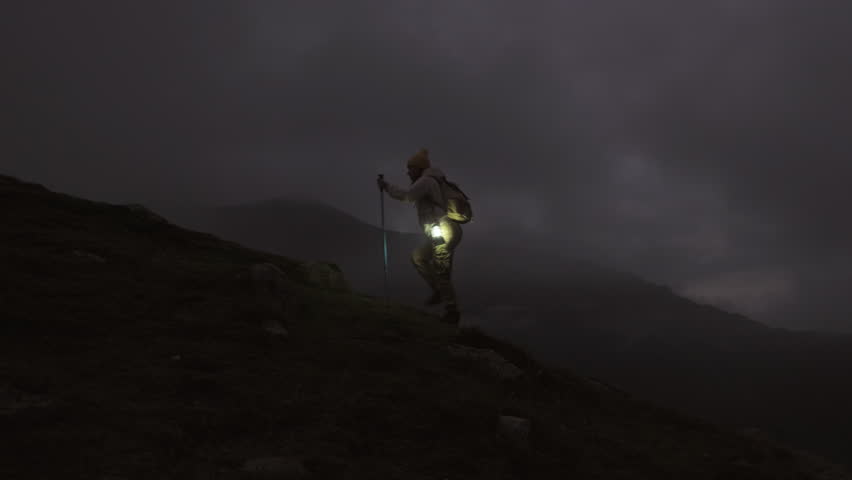 Woman hiker climbs mountain in evening twilight in foggy haze, captivating cinematic shot.