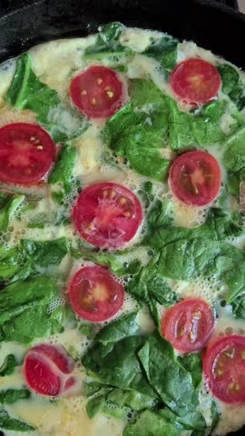 cooking an omelet with spinach and cherry tomatoes in a frying pan on the stove