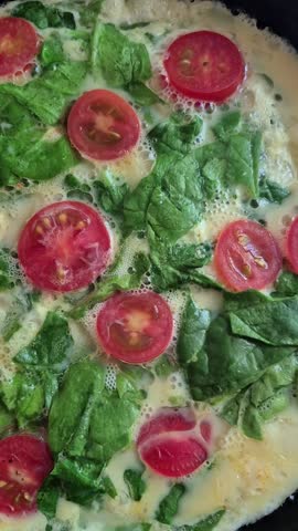 cooking an omelet with spinach and cherry tomatoes in a frying pan on the stove