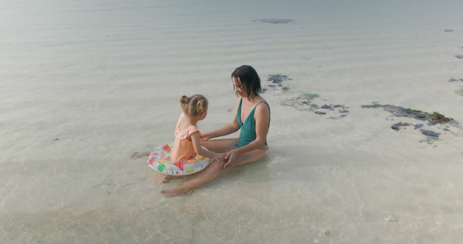 Mother with her cute little daughter playing in ocean water on beach. Happy family on holidays